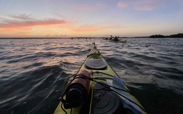 a kayak points to the sun as its sets over water